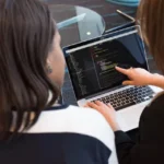 Developer using best coding ai agent on laptop in modern workspace with dual monitors displaying code and AI chat interface