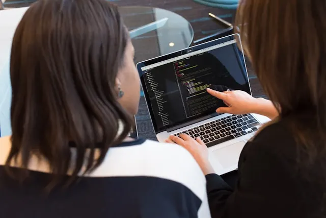 Developer using best coding ai agent on laptop in modern workspace with dual monitors displaying code and AI chat interface